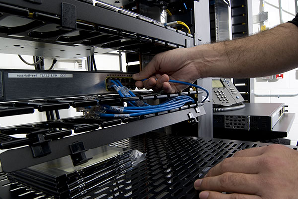 Picture of a man plugging in blue wires into a server