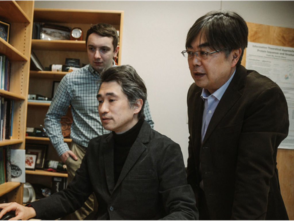 Three men look at a computer screen